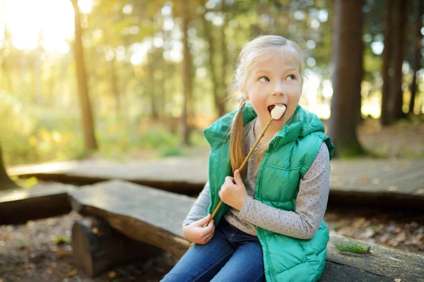 Schattig jong meisje roosteren marshmallows op stok bij vreugdevuur. Kind plezier in kampvuur. Kamperen met kinderen in Fall forest. — Stockfoto