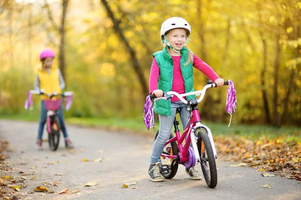 Irmãzinhas bonitas andando de bicicleta em um parque da cidade no dia ensolarado de outono. Lazer familiar ativo com crianças . — Fotografia de Stock