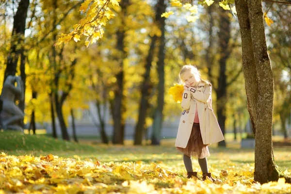 Adorabile ragazza che si diverte nella bella giornata autunnale. Bambino felice che gioca nel parco autunnale. Ragazzo raccolta fogliame caduta gialla . — Foto Stock
