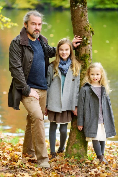 Father and his two pretty daughters having fun in autumn park. Parent and two kids enjoying themselves on warm fall day in city park. — Stock Photo, Image
