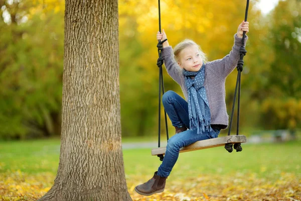 Aranyos fiatal lány birtoklás móka-ra egy hinta, napsütéses őszi parkban. Családi hétvége a városban. — Stock Fotó