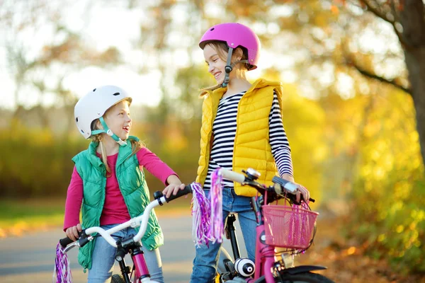 Carino sorelline in sella alle biciclette in un parco cittadino nella soleggiata giornata autunnale. Tempo libero famiglia attiva con i bambini . — Foto Stock