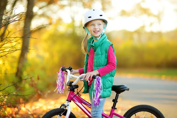 Симпатичная маленькая девочка катается на велосипеде в городском парке в солнечный осенний день. Активный семейный отдых с детьми . — стоковое фото