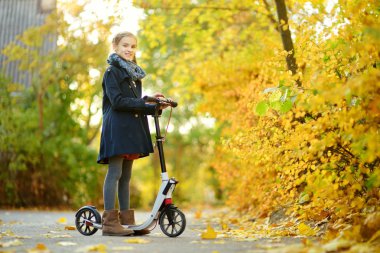 Sevimli genç kız güneşli sonbahar akşamı bir şehir parkında onu scooter sürme. Pretty preteen çocuk bir rulo sürme.