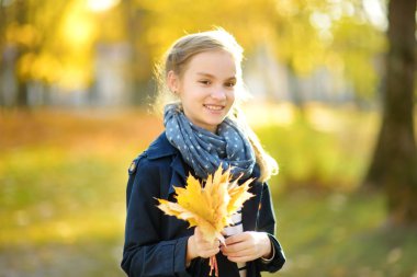 Güzel sonbahar gününde eğlenen sevimli genç kız. Sonbahar parkında oynayan mutlu çocuk. Sarı sonbahar yaprakları toplayan çocuk.