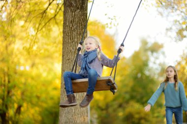Sevimli genç kız güneşli sonbahar parkta bir salıncak ta eğleniyor. Bir şehirde aile hafta sonu.