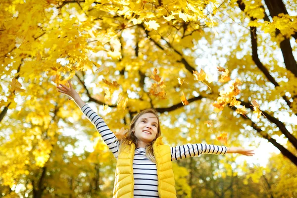 Очаровательная молодая девушка веселится в прекрасный осенний день. Счастливый ребенок играет в осеннем парке. Ребенок собирает желтую осеннюю листву . — стоковое фото