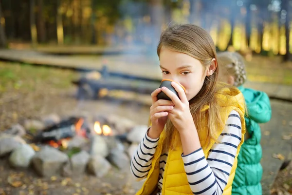 Roztomilá mladá dívka pije čaj a prabí Marshmallow na palbě. Dítě se baví v táboráku. Kempování s dětmi v padinském lese. — Stock fotografie