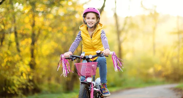Adorable young girl riding a bike in a city park on sunny autumn day. Active family leisure with kids. — Stock Photo, Image