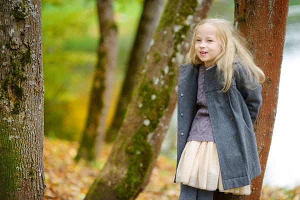 Urocza młoda dziewczyna bawią się na pięknym jesiennym dniu. Szczęśliwe dziecko bawiąc się w jesiennym parku. Dziecko zbierające żółte jesienne liście. — Zdjęcie stockowe