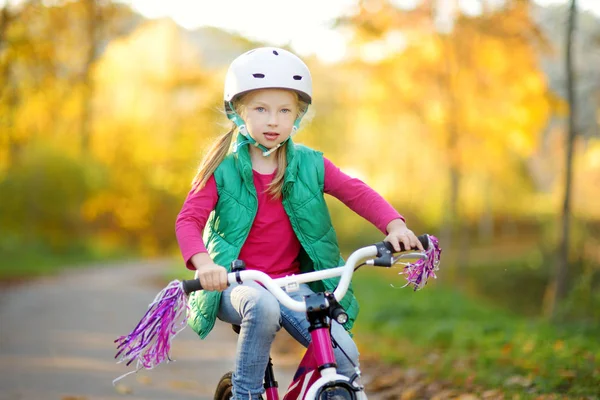Cute little girl riding a bike in a city park on sunny autumn day. Active family leisure with kids. — Stock Photo, Image