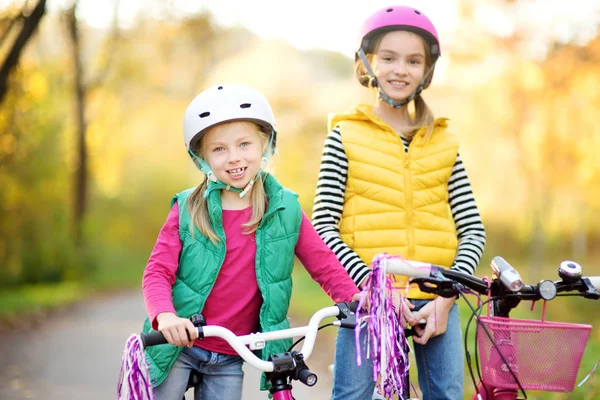 Güneşli sonbahar gününde bir şehir parkında bisiklete binen sevimli kız kardeşler. Çocuklarla aktif aile eğlencesi. — Stok fotoğraf