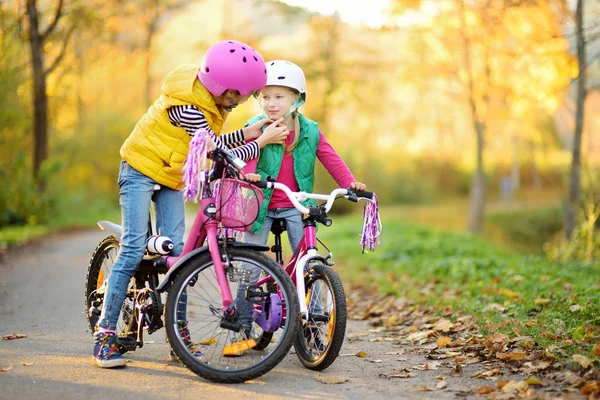 Милые сестрички катаются на велосипедах в городском парке в солнечный осенний день. Активный семейный отдых с детьми . — стоковое фото