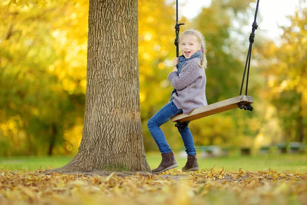 Cute młoda dziewczyna zabawy na huśtawce w słonecznym jesiennym parku. Rodzinny weekend w mieście. — Zdjęcie stockowe