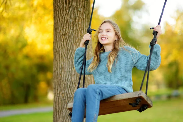 Cute young girl having fun on a swing in sunny autumn park. Family weekend in a city. — Stock Photo, Image
