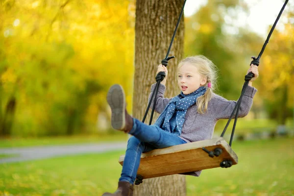 Sevimli genç kız güneşli sonbahar parkta bir salıncak ta eğleniyor. Bir şehirde aile hafta sonu. — Stok fotoğraf