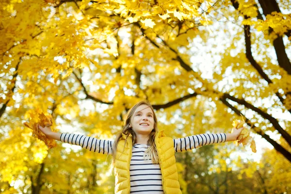 Schattig jong meisje plezier op mooie herfst dag. Gelukkig kind spelen in herfst Park. Kid verzamelen gele val loof. — Stockfoto