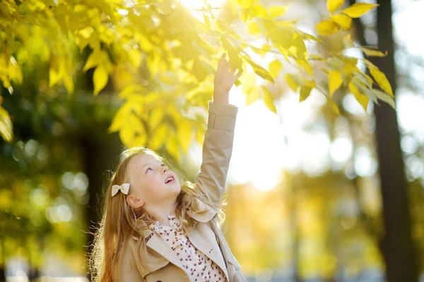 Adorabile ragazza che si diverte nella bella giornata autunnale. Bambino felice che gioca nel parco autunnale. Ragazzo raccolta fogliame caduta gialla . — Foto Stock