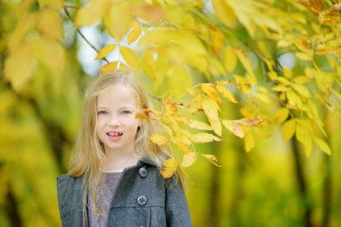 Güzel sonbahar gününde eğlenen sevimli genç kız. Sonbahar parkında oynayan mutlu çocuk. Sarı sonbahar yaprakları toplayan çocuk.