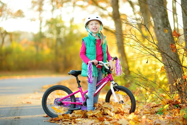 Carina bambina in bicicletta in un parco cittadino nella soleggiata giornata autunnale. Tempo libero famiglia attiva con i bambini . — Foto Stock