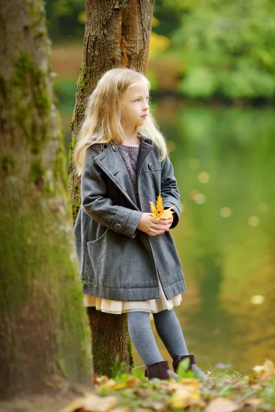 Güzel sonbahar gününde eğlenen sevimli genç kız. Sonbahar parkında oynayan mutlu çocuk. Sarı sonbahar yaprakları toplayan çocuk. — Stok fotoğraf