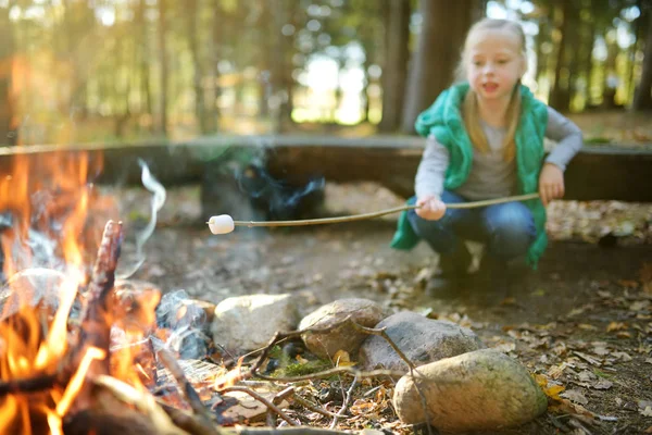 Urocza młoda dziewczyna prażenie marshmallows na kij na ognisko. Dziecko bawią się ogniem obozu. Kemping z dziećmi w lesie jesienne. — Zdjęcie stockowe