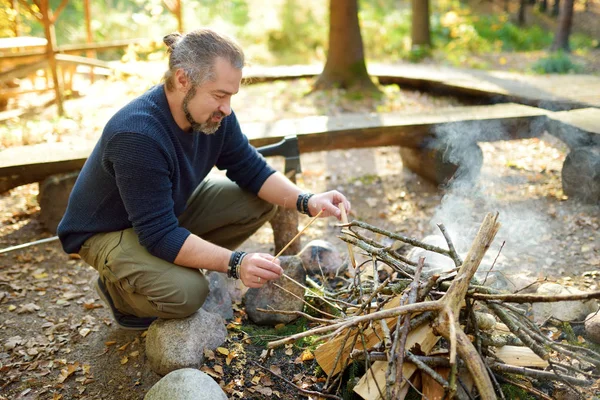 Un joven encendiendo una hoguera. Turista masculino haciendo un fuego. Caminante divirtiéndose en el fuego del campamento. Camping en bosque de otoño . — Foto de Stock