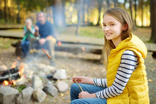 Niedliche kleine Schwestern und ihr Vater braten Marshmallows am Lagerfeuer. Kinder haben Spaß am Lagerfeuer. Zelten mit Kindern im Herbstwald. — Stockfoto
