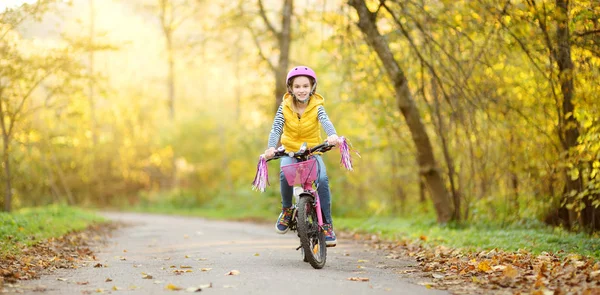 Güneşli sonbahar gününde bir şehir parkında bisiklete binen sevimli genç kız. Çocuklarla aktif aile eğlencesi. — Stok fotoğraf