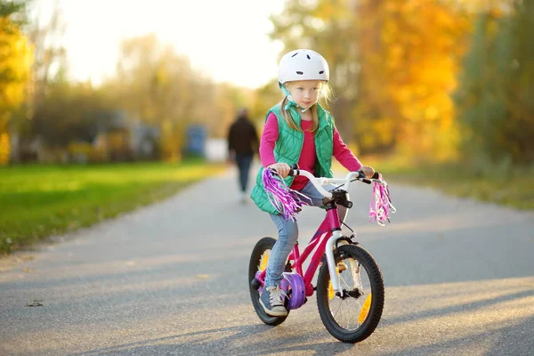 Sevimli küçük kız güneşli sonbahar gününde bir şehir parkında bisiklete biniyor. Çocuklarla aktif aile eğlencesi. — Stok fotoğraf