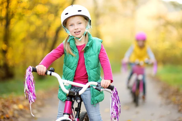 Cute little sisters riding bikes in a city park on sunny autumn day. Active family leisure with kids. — Stock Photo, Image