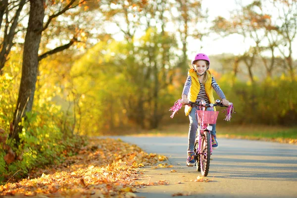 Adorable young girl riding a bike in a city park on sunny autumn day. Active family leisure with kids. — Stock Photo, Image