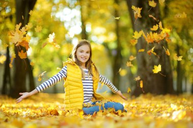 Güzel sonbahar gününde eğlenen sevimli genç kız. Sonbahar parkında oynayan mutlu çocuk. Sarı sonbahar yaprakları toplayan çocuk.