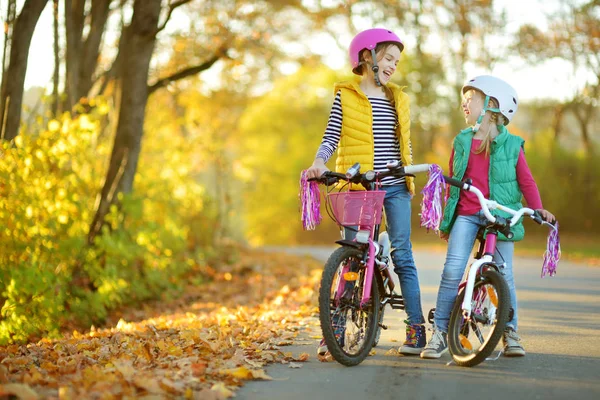 Cute little sisters riding bikes in a city park on sunny autumn day. Active family leisure with kids. — Stock Photo, Image