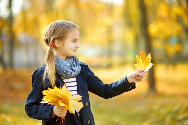 Imádnivaló fiatal lány birtoklás móka-ra szép őszi napon. Boldog gyermek játszik az őszi parkban. Gyerek összegyűjtése sárga Lombhullás. — Stock Fotó