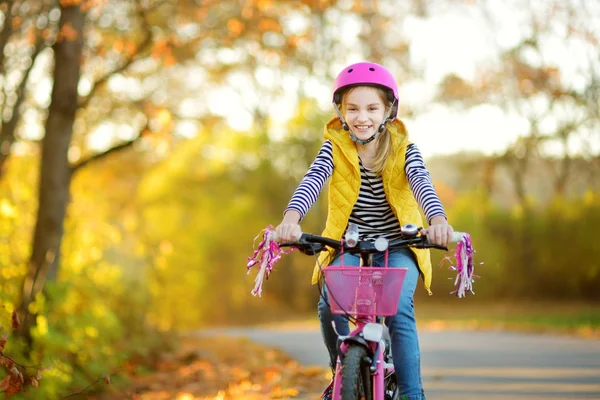 Adorable young girl riding a bike in a city park on sunny autumn day. Active family leisure with kids. — Stock Photo, Image