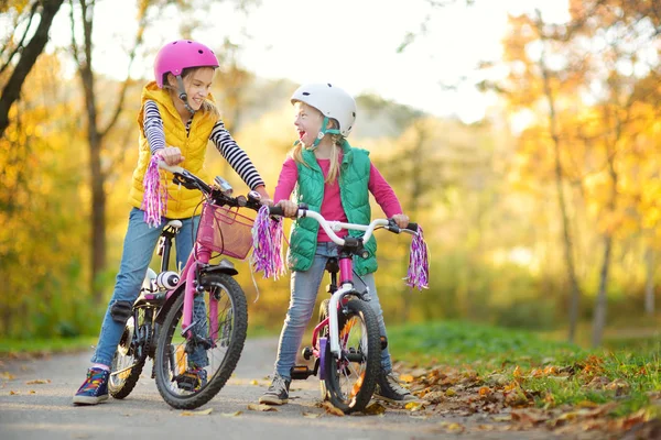 Güneşli sonbahar gününde bir şehir parkında bisiklete binen sevimli kız kardeşler. Çocuklarla aktif aile eğlencesi. — Stok fotoğraf