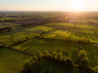 İrlanda'nın uçsuz bucaksız yemyeşil otlaklarının ve tarım arazilerinin havadan görünümü. Yeşil alanlar ve çayırları ile güzel İrlandalı kırsal. Gün batımında kırsal manzara.