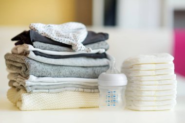 Bir yığın bebek giysisi, tek kullanımlık bebek bezi ve bir biberon. Ebeveyn masrafları konsepti. Bebek bütçesi hazırlıyorum. Yeni doğmuş bir bebek için para biriktiriyorum. Yeni bir bebek için bütçe ayırıyorum..