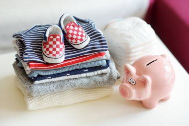 Bebek kıyafetleri, tek kullanımlık bebek bezleri ve kumbarası. Ebeveyn masrafları konsepti. Bebek bütçesi hazırlıyorum. Yeni doğmuş bir bebek için para biriktiriyorum. Yeni bir bebek için bütçe ayırıyorum..