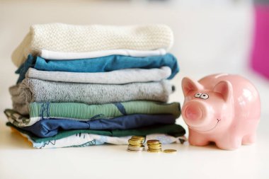 Bebek kıyafetleri, bozuk paralar ve kumbara yığını. Ebeveyn masrafları konsepti. Bebek bütçesi hazırlıyorum. Yeni doğmuş bir bebek için para biriktiriyorum. Yeni bir bebek için bütçe ayırıyorum..