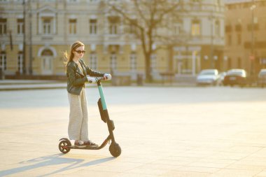 Güneşli bahar gününde elektrikli scooterla gezen tatlı bir genç kız. Vilnius, Litvanya 'da elektrikli şehir ulaşımı. Kiralık scooter 'lar. Çocuklarla aile eğlencesi..