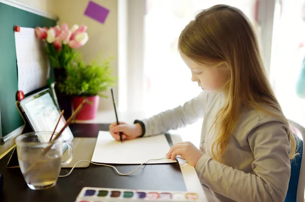 若い女子高生は家でデジタルタブレットを使って宿題をしている ガジェットを使って勉強する子供 子供のための教育と距離学習 隔離中のホームスクーリング ホームエンターテイメントに滞在する — ストック写真
