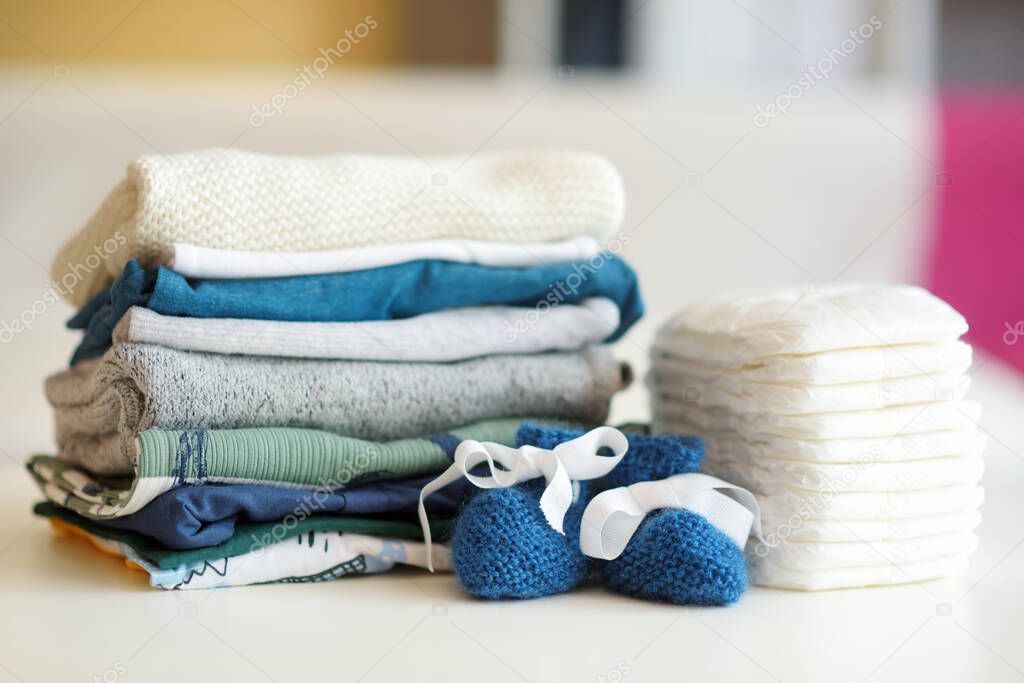 A pile of baby clothes, disposable diapers and little shoes. Parenting expenses concept. Working out a baby budget. Saving money when planning for a newborn. Budgeting for a new baby.