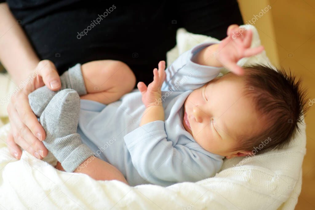 Cute little newborn baby boy sleeping in his mothers arms. Portrait of tiny new baby at home. Adorable son being held by his mommy. New bundle of joy.