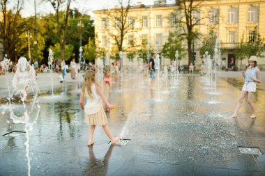 Litvanya 'nın Vilnius kentindeki yeni yenilenmiş Lukiskes Meydanı' ndaki çeşmelerde oynayan şirin kız kardeşler. Çocuklar güneşli yaz gününde suyla eğleniyorlar. Çocuklar için aktif boş zaman.