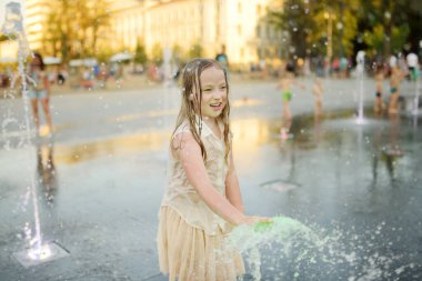 Litvanya 'nın Vilnius kentindeki yeni yenilenmiş Lukiskes Meydanı' ndaki çeşmelerde oynayan tatlı genç kız. Güneşli yaz gününde çocuk suyla eğleniyor. Çocuklar için aktif boş zaman.