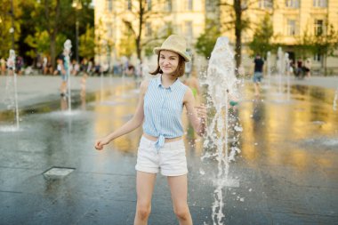 Litvanya 'nın Vilnius kentindeki yeni yenilenmiş Lukiskes Meydanı' ndaki çeşmelerde oynayan tatlı genç kız. Güneşli yaz gününde çocuk suyla eğleniyor. Çocuklar için aktif boş zaman.