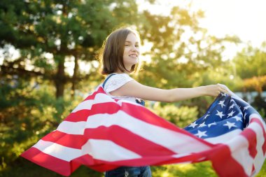 Güzel bir yaz gününde elinde Amerikan bayrağı tutan sevimli genç bir kız. Bağımsızlık Günü konsepti. Ulusal bayramı kutlayan çocuk. Anma Günü.