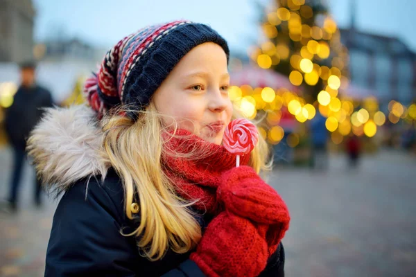 ラトビアのリガで伝統的なクリスマスフェアにストライプロリポップを持っているかわいい女の子 クリスマスマーケットでお菓子やキャンディー ジンジャーブレッドを楽しむ子供たち 家族や子供と冬の時間 — ストック写真